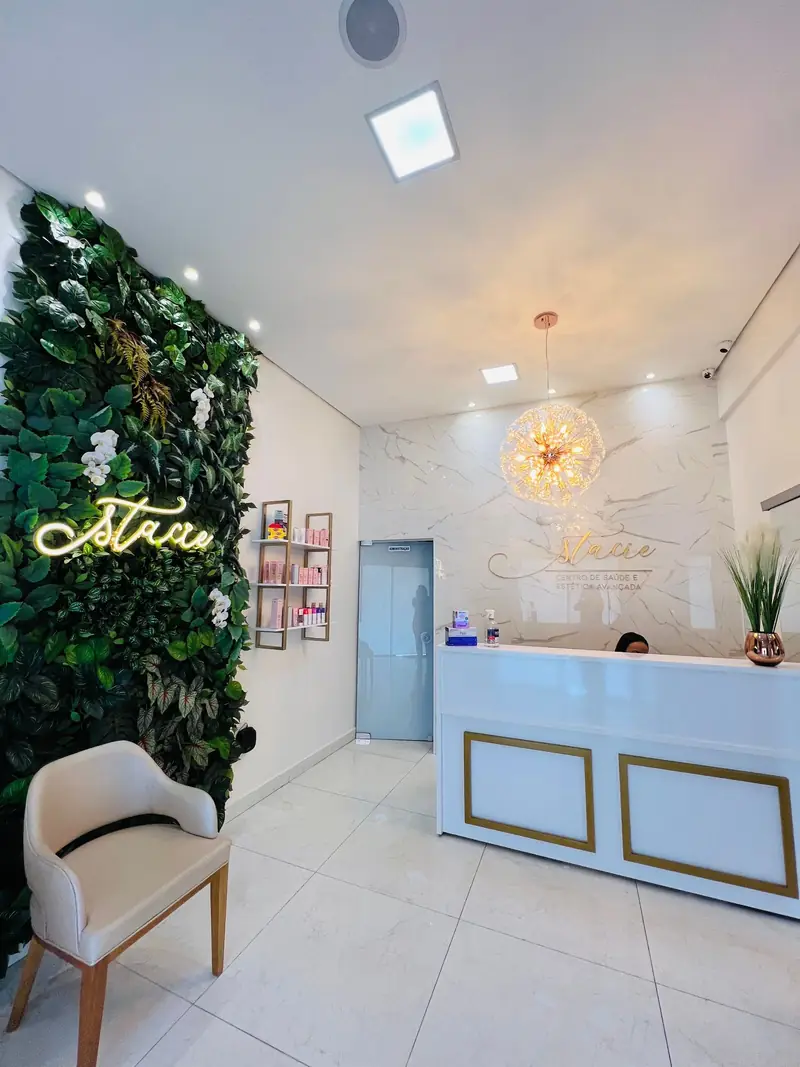 Recepção da Stacie: parede verde com neon, lustre de cristal e balcão branco com dourado