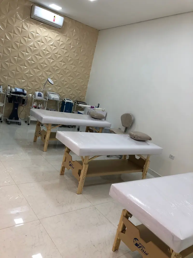 Sala de procedimentos com macas brancas, parede 3D e equipamentos de estética